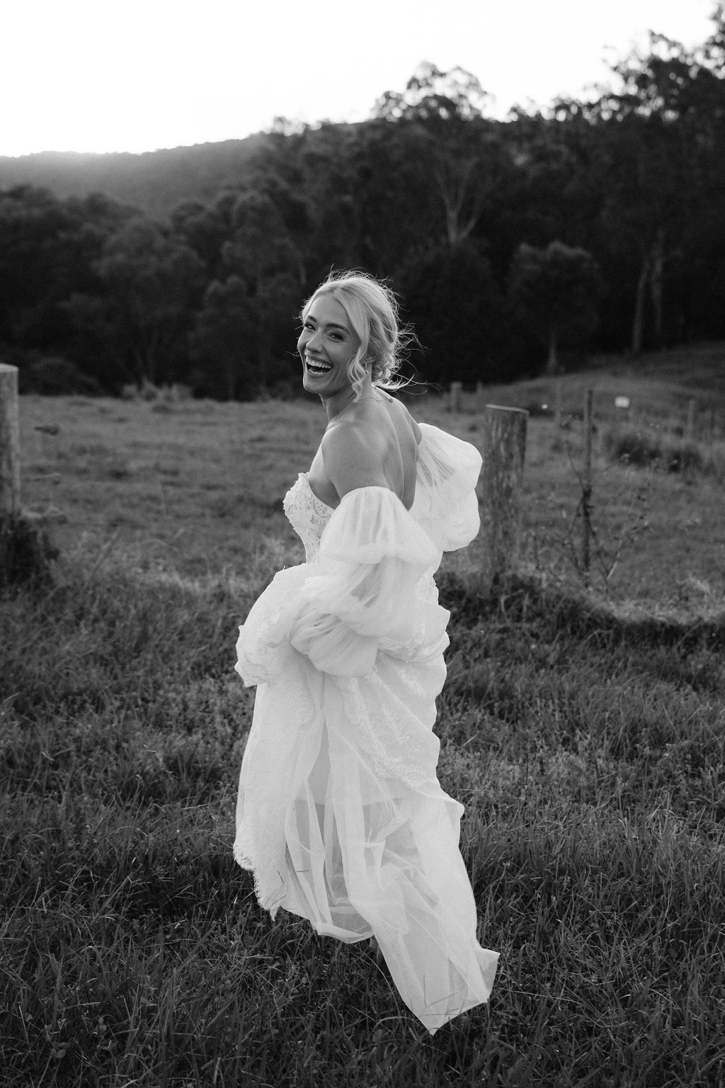 Black and white image of bride in wedding dress looking back as she frolics across the lawn in the Sunshine Coast hinterland town of Maleny