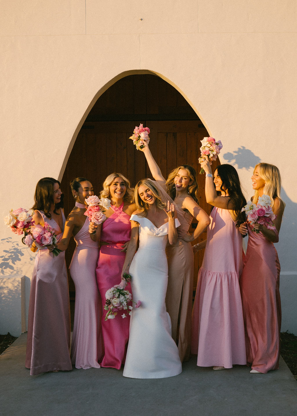 Bride and bridesmaids wearing pink dresses in various styles and shades of pink. 