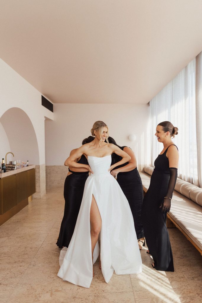 Bridesmaids assisting bride to get dressed in wedding gown