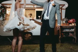 bride and groom dancing at their outdoor wedding reception with vintage caravan bar in the background