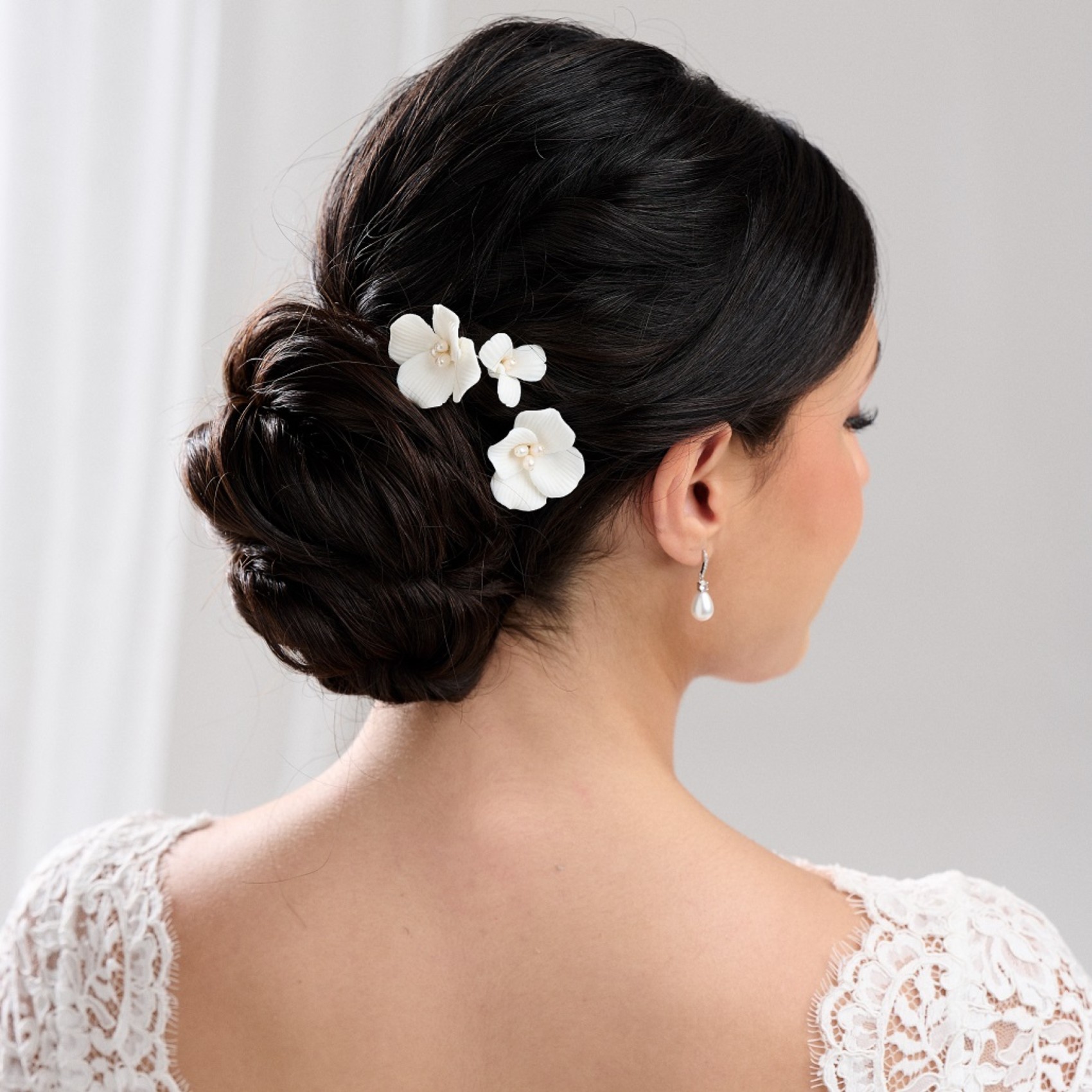 close up of brunette bride with upstyle wearing white floral hairpiece with pearls