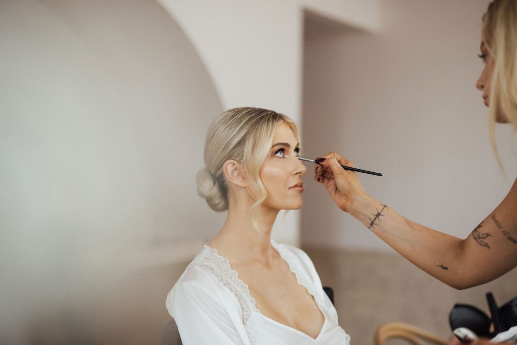 Bride getting makeup done on wedding day morning wearing white bridal robe