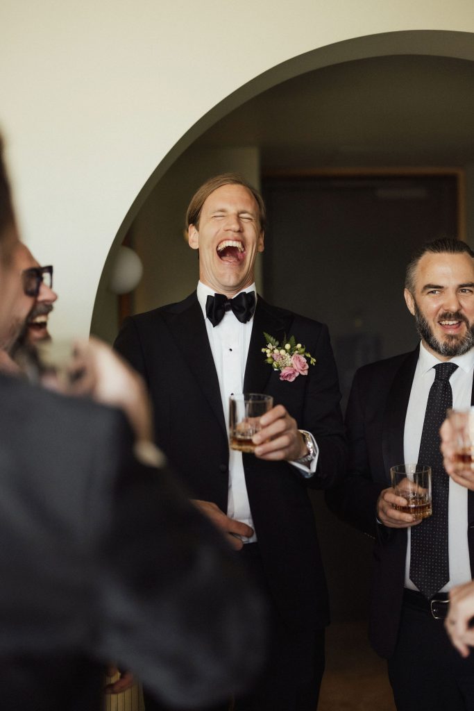 Groom and groomsmen having a laugh and whiskey before wedding ceremony