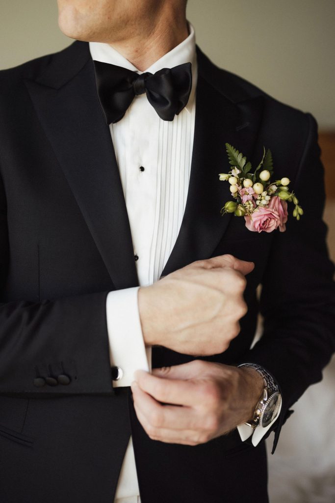 Torso of groom in tuxedo putting on his cufflinks