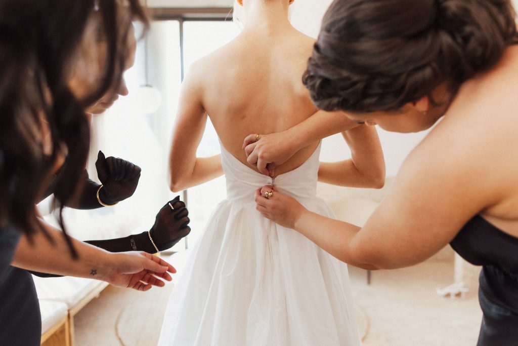 Bridesmaids assisting bride to get dressed in wedding gown