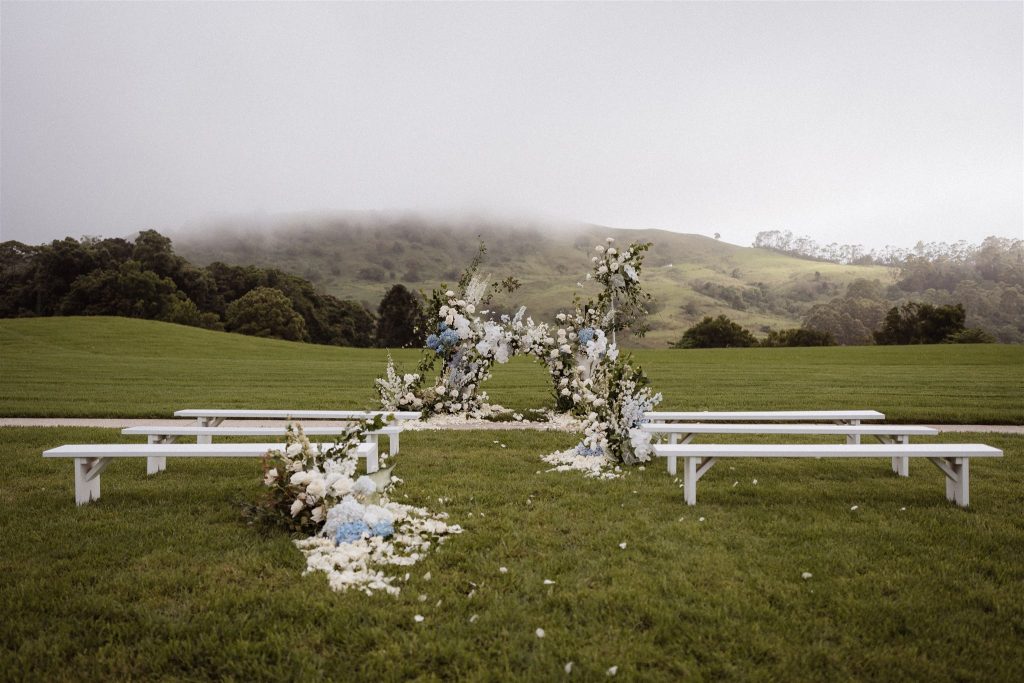 Ceremony styling with white bench seats and blue and white florals. 