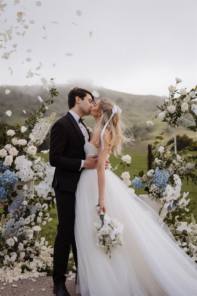 Couple kissing at wedding ceremony with blue and white wedding floral ceremony flowers in Maleny